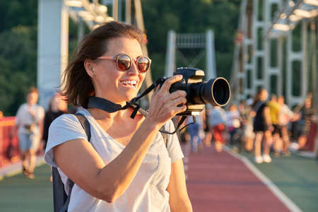 Mature woman photographer with camera taking photo picture. Female blogger, freelancer working with smile and enjoymentの写真素材