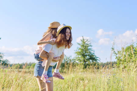 Happy children two girls sisters teenager and younger laughing and having fun in meadow, blue sky, summer nature. Active healthy lifestyle, friendly family, happy childhood, copy spaceの写真素材