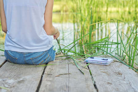 Young woman sitting with her back on wooden pier, enjoying picturesque view of lake water, relaxing in nature on sunny summer day, copy spaceの写真素材