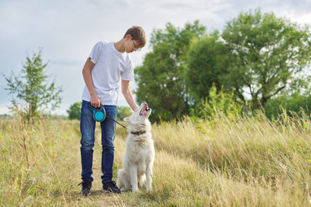 Outdoor portrait of boy with white dog. Friendship of teenager with pet, boy walking in summer...