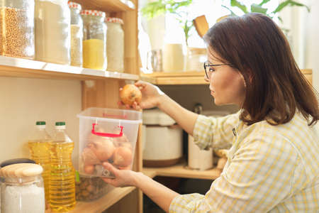 Woman in pantry taking onions, food storage in pantry on wooden shelf.の写真素材