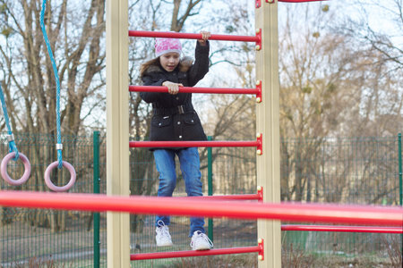 Girl child of 8, 9 years old on outdoor sports equipment, childrens playground. Spring season, girl...