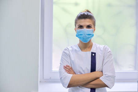 Portrait of confident young female medic in medical mask with folded arms over clinic interiors, copy spaceの写真素材