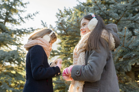 Outdoor winter portrait of two little girls smiling and having fun near the Christmas tree, golden...