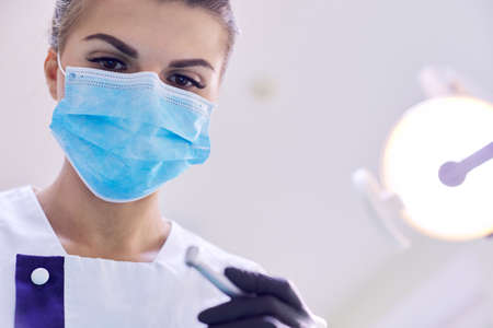 Female dentist treating teeth to patient, close-up face of doctor in mask with healing tools, copy spaceの写真素材