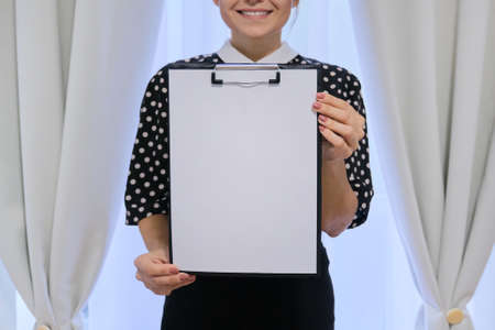 Mature smiling successful business woman showing blank paper on clipboard. Female housewife near window, place for your text, copy spaceの写真素材