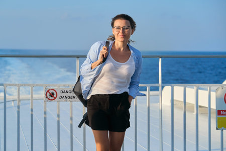 Woman on deck of ferry, female standing in strong wind, enjoying sea travel, sunset at sea, copy...