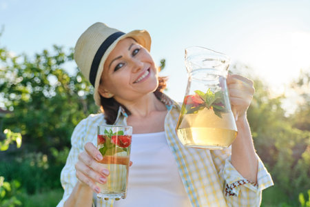 Smiling woman with jug of refreshing natural homemade drink in the summer garden, herbal tea with...
