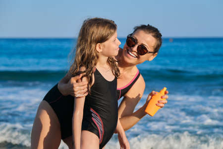 Mother applying sunblock to daughter on beach, parent and child resting at seaside resort, protecting skin from sunburnの写真素材