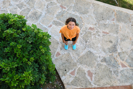 Smiling teenager girl looking up in camera, top view. Sunny summer day, female standing on gray...