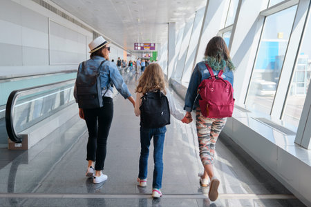 Airport terminal inside, walking people passengers with luggage. Family mother and daughters with backpacks holding hands togetherの写真素材