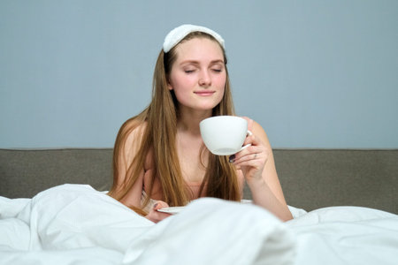 Beautiful young woman 20 years old blonde in bed with cup of tea, morning, white bed, background...