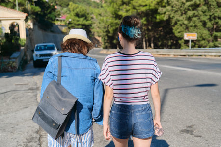 Two women mother and daughter teenager walking on sunny summer day on mountain road. Tourism,...