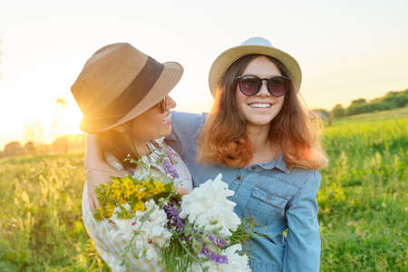 Mothers day, hugging happy smiling teenager daughter with mother in meadow with bouquet of spring flowersの写真素材