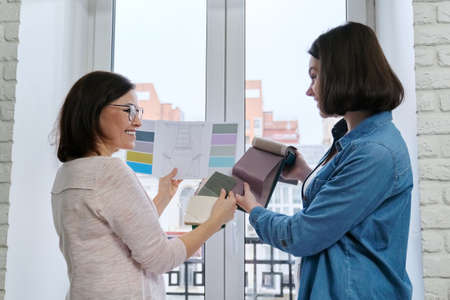 Two women designers working with fabric samples for interior. Choosing fabrics for curtains, furniture upholstery, calculating costの写真素材