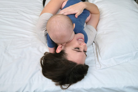 Portrait of beautiful young mother and her baby 7 month old son, parent and baby lying in bed...