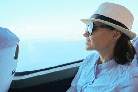 Woman passenger in hat sitting in bus looking out the window, tourist transportation, sky and sea in...