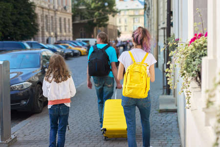 Children two girls daughters and father, tourists walking around city with backpacks and a suitcase. Travel, family, vacation, tourism, summer conceptの写真素材