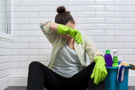 Tired woman doing house cleaning in bathroom. Female in gloves with detergents, bucket sitting on floor. Fatigue, stress, cleanliness, homeの写真素材