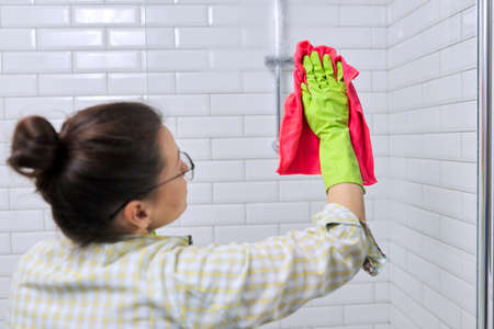 Woman doing cleaning in the bathroom, at home. Female cleaning polishing shower glass with a washcloth with microfiber.の写真素材