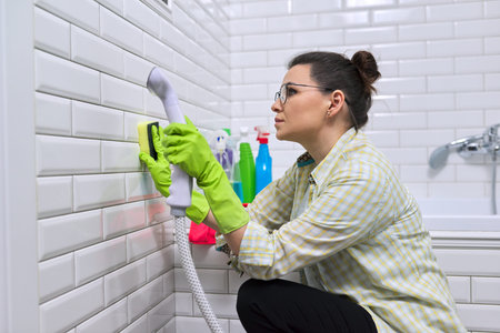 Woman doing bathroom cleaning at home, female washing tile wall with steam. Using steam cleaner for...