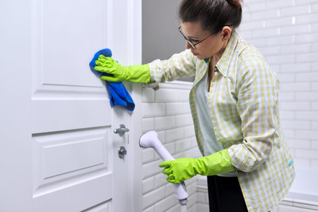 Woman housewife doing house cleaning in bathroom, female washing door with shower steam. Using steam...