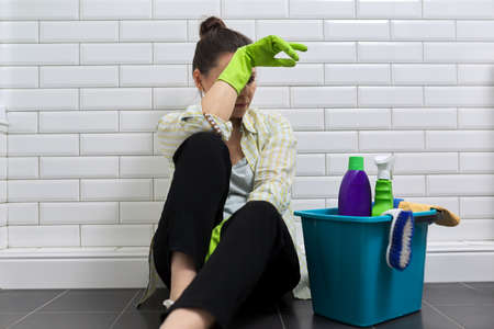 Tired woman doing house cleaning in bathroom. Female in gloves with detergents, bucket sitting on floor. Fatigue, stress, cleanliness, homeの写真素材