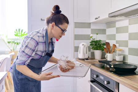 Woman housewife in apron preparing pork in baking sleeve at home, puts tray of meat in the ovenの写真素材