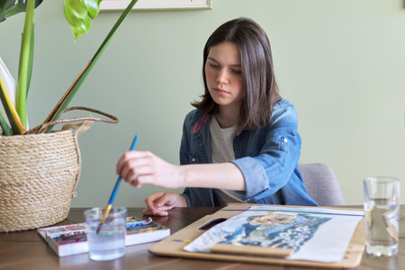 Teenager girl painting with watercolors, sitting at home at the table. Art, education, creativity,...
