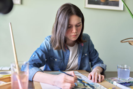 Teenager girl painting with watercolors, sitting at home at the table. Art, education, creativity,...