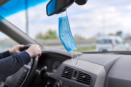 Protective medical mask of the driver in the car, man's hands on the steering wheel of moving...