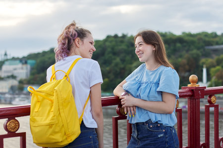 Portrait of two teenage girls standing on bridge over river, friends walk on summer sunny day....