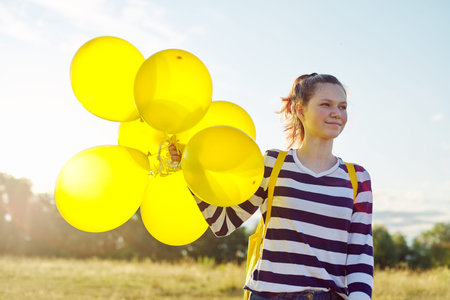 Portrait of happy teenager girl 15 years old with yellow balloons. Sky in clouds, nature background. Holiday, nature, teens, joy conceptの写真素材