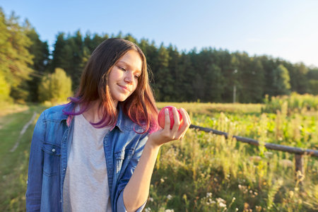 Beautiful teenager girl with red apple, happy young woman on nature, scenic sunset landscape...