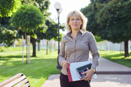 Outdoor portrait of business confident middle-aged woman, beautiful female with business papers...