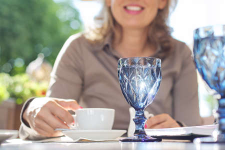 Outdoor restaurant, woman with glass of water, drink, wine. Beautiful glass goblet of blue colorの写真素材