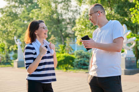 Couple of adult people resting talking after sports exercises, jogging in the park. Active healthy lifestyle, sport, fitness in middle-aged peopleの写真素材