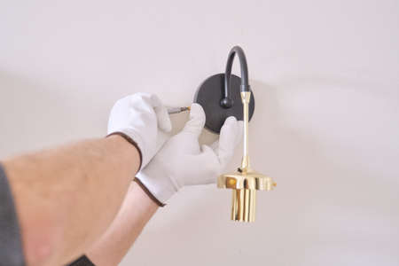 Close-up hands of electrician installing wall lamp.の写真素材