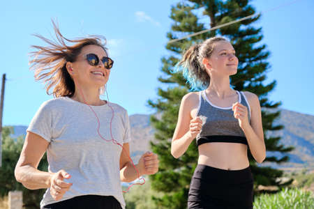 Active athletic family, mother and teenage daughter running together on an outdoor road. Healthy lifestyle, sport, communication of parent and child teenagerの写真素材