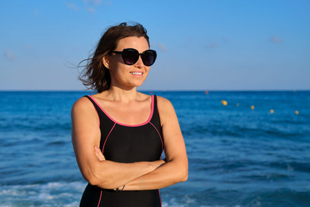 Portrait of mature smiling beautiful woman in sunglasses swimsuit enjoying sea sunset, vacation,...