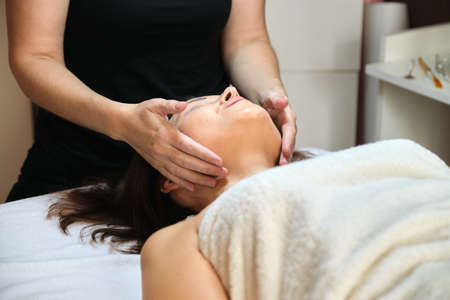 Middle age woman in beauty spa salon, lying on massage table. Close up face and neck massage. Body and face care, healthcare, treatment, cosmetology, mature womenの写真素材