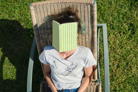Tired teenager student asleep on sunbed with book. Sleeping girl on sunny day, on green lawn in...
