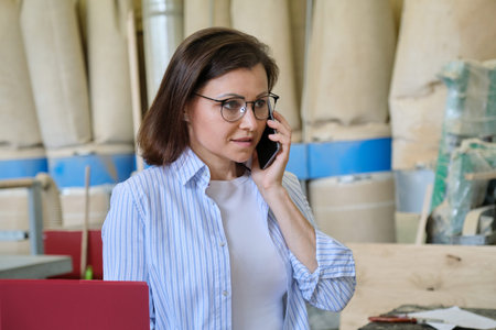 Business portrait of mature woman talking on smartphone at workplace. Industrial business, carpentry...