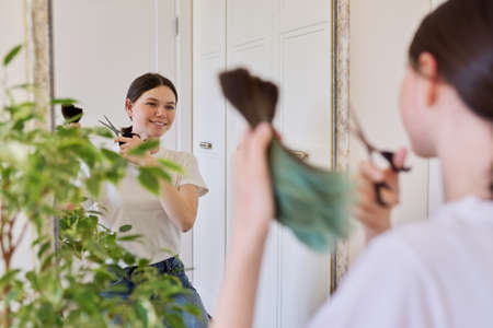 Girl makes a haircut at home, teenager cut her hair, in hands bunch of cut hair and scissors, cut dyed unhealthy hairの写真素材