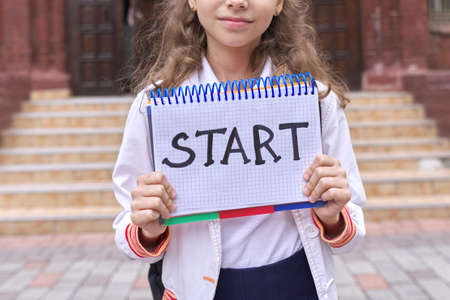 Elementary school girl student with notepad and handwritten word start, school building background. Back to school, education conceptの写真素材
