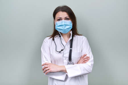 Portrait of confident mature doctor woman in medical protective mask with stethoscope. General practitioner, medical care, medicine, female posing on light green backgroundの写真素材