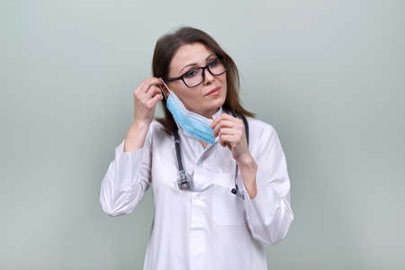 Woman doctor with stethoscope puts on medical protective mask. General practitioner, medical care, medicine, female posing on light green backgroundの写真素材