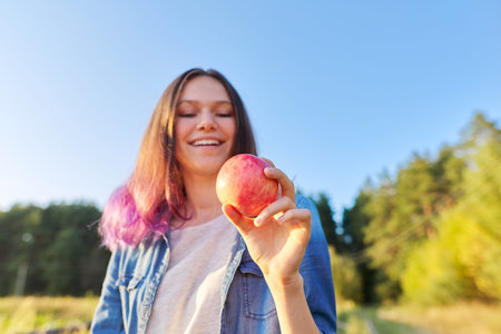 Young happy woman with red apple, girl biting an apple, sunset natural landscape background, healthy...