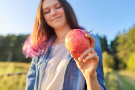 Young happy woman with red apple, girl biting an apple, sunset natural landscape background, healthy natural foodの写真素材