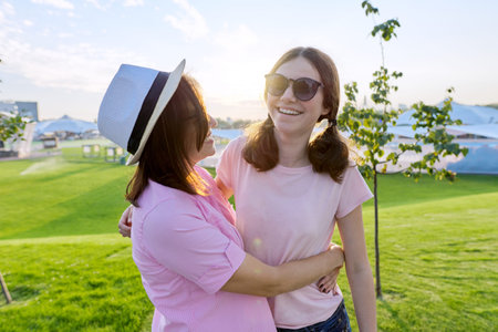 Mothers day, happy smiling hugging mother and teenager daughter. Outdoor green lawn sunset...